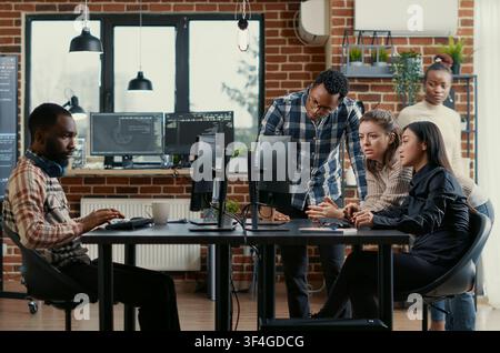 Junior developers asking senior programmer for algorithm help in a software office, showing source code, programming workflow and technical collaboration on digital development tasks. Stock Photo