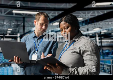 Team of data center system administrators scanning equipment for errors using devices. Server farm colleagues working together, backing up supercomputers data using software on laptop Stock Photo
