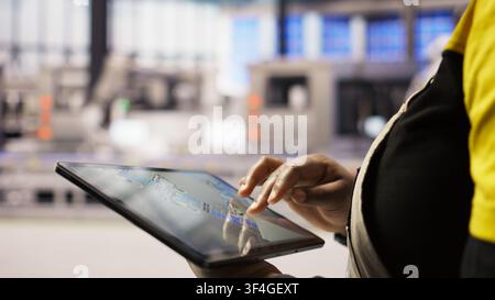 Close up of engineer in industry 4.0 plant designing robotic production lines using CAD application on tablet. Smart factory specialist uses software to optimize floor layouts, camera A Stock Photo