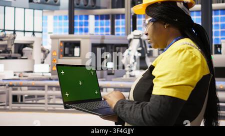Technician in industrial plant using green screen laptop to diagnose equipment errors. Factory specialist using chroma key mockup notebook to coordinate repair tasks on assembly lines, camera A Stock Photo