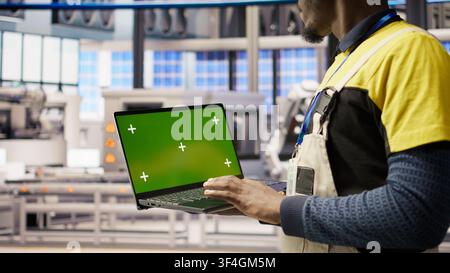 Smart factory mechanic testing automated systems using isolated screen laptop, doing maintenance. Industry 4.0 plant serviceman inspecting equipment using mockup notebook to identify errors, camera A Stock Photo