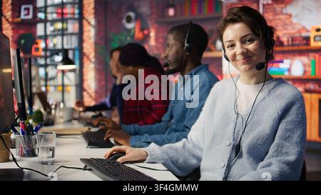 Happy call center employee working on PC, doing account management in office. Cheerful customer support agent handling inbound calls, assisting customers with inquiries, camera B close up Stock Photo