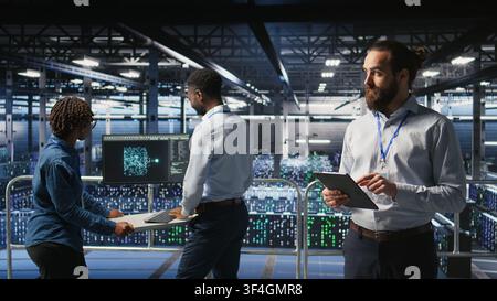 Technicians on data center platform using devices to monitor neural network LLM visualization. Industrial server hub engineering team overseeing rigs powering machine learning processes, Stock Photo
