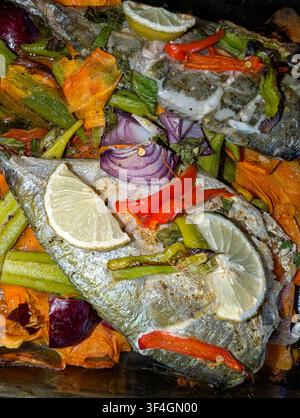 A freshly baked fish dish, cooked with vegetables including carrots, peppers, red onions, okras, tomatoes and garnished with slices of lime. Stock Photo