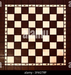 A flat lay, top-down view of an empty classic wooden chessboard. Features alternating light and dark brown squares surrounded by a frame with clear algebraic notation (numbers 1-8 and letters A-H). Ideal clean backdrop for board game design, strategy concepts, and background copy space. Stock Photo