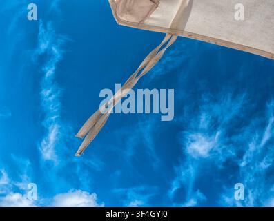 A beige beach umbrella positioned against a bright blue sky. Stock Photo