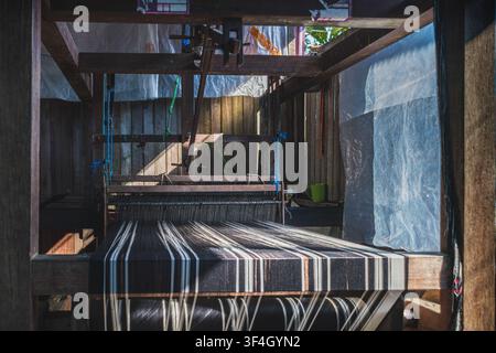 A close-up shot of an authentic wooden handloom threaded with black and white striped yarn inside a rustic workshop. Stock Photo
