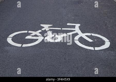 This is a close-up shot of a clear white bicycle lane symbol painted on an urban asphalt road. The symbol, outlined in clean white lines that form the Stock Photo