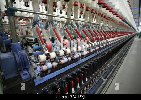 This is a close-up shot focusing on the spinning equipment inside a modern textile factory. The groups of spinning spindles and red-blue mechanical co Stock Photo