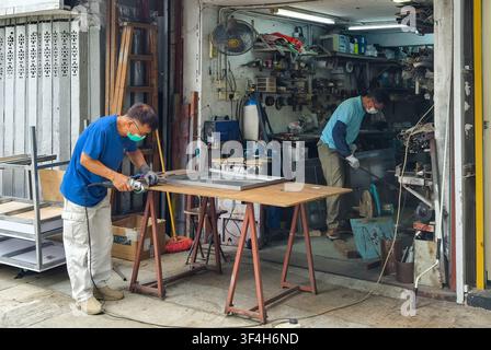 Two craftsmen working in a small metal fabrication and welding workshop in Hong Kong Stock Photo