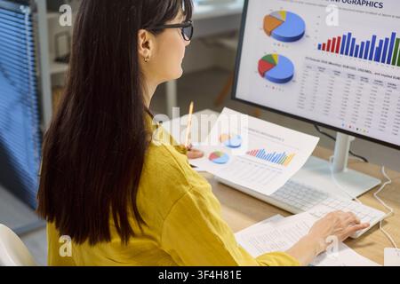 Businesswoman analyzing financial charts on computer monitor in modern office Stock Photo