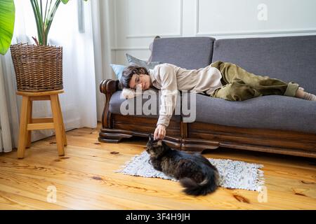 Tranquil relaxed woman comfortably lying on couch enjoying lazy day and time with domestic cat. Stock Photo