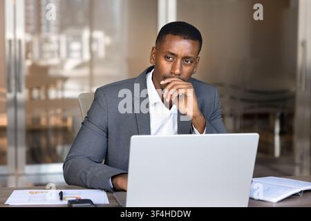 Thoughtful African businessman sitting at office desk working on laptop Stock Photo