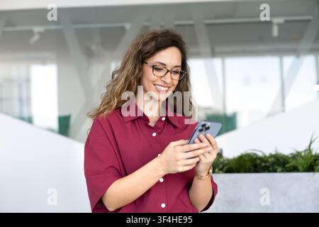 Young adult businesswoman checking smartphone in corporate office Stock Photo