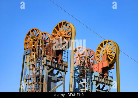 The image focuses on the top wheel structures of multiple tower-type pump jacks. The large orange-red mechanical wheels contrast sharply with the blue Stock Photo