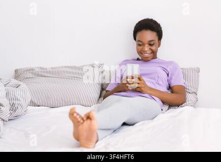 Surfing in internet at home. Girl is lying on bed and using smartphone Stock Photo