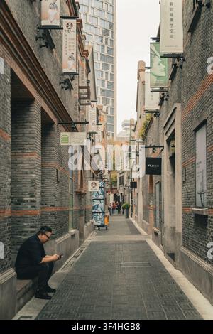 Man sitting on street using smartphone in narrow historic brick alley, Xintiandi, Shanghai Stock Photo