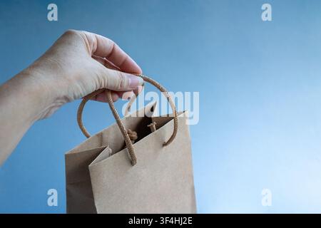 Hand holding a brown color paper shopping bag. Isolated on blue background. Stock Photo