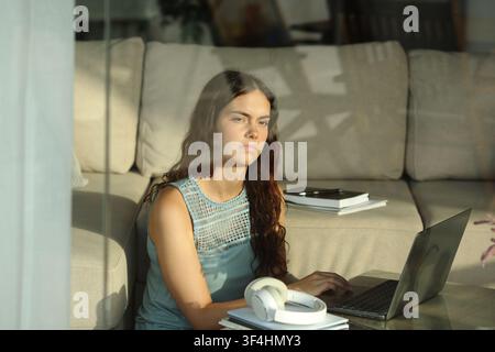 Pensive and distracted serious student looking through a window at home Stock Photo
