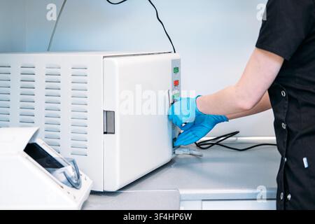 Gloved hand presses button on control panel of autoclave sterilizer machine in clinical setting. Pressing start button autoclave, dental worker Stock Photo