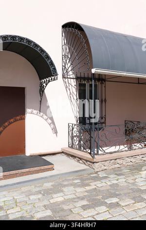 Elegant entrance of old town building featuring classic wrought iron canopies and ornate metal window grills. Architectural details create beautiful Stock Photo