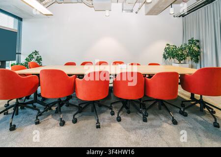 Empty conference room red chairs business recruitment meeting, showing a long wooden board table surrounded by bright red office armchairs with no peo Stock Photo