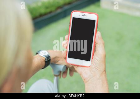 Rear view of senior man with walking cane using mobile phone with copy space. Old man holding a cell phone at outdoor. Concept of online communication Stock Photo
