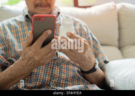 Concerned senior man read bottle label while using his smart  phone to research a medication or health information. Selective focus, close-up. Stock Photo