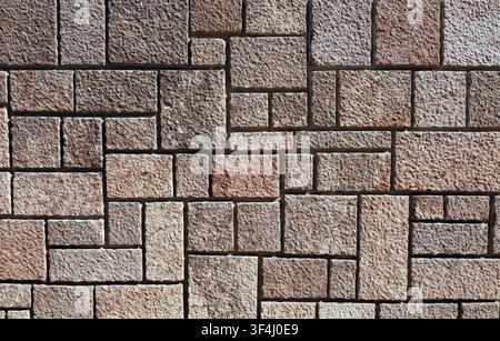 Wall made of reconstructed stone tiles imitating granite rock. Colors are warm shades that range from light brown to pink and gray. Rustic coating Stock Photo