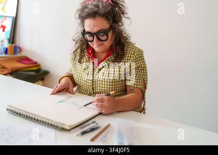 Woman designer engrossed in her creative process, drawing unique ideas in a sketchbook with various art supplies on a white desk Stock Photo