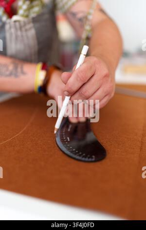 Hand drawing intricate patterns on brown fabric using a ruler and pencil, crafting designs for production Stock Photo