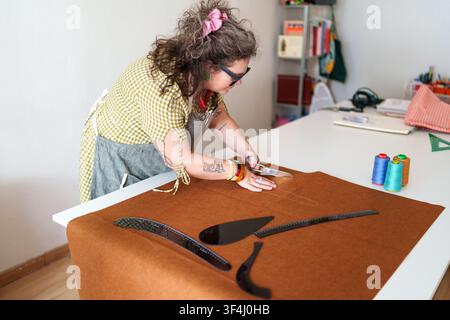 Craftswoman meticulously cutting textile felt, creating custom clothing with tailoring rulers and spools of thread on a white table Stock Photo