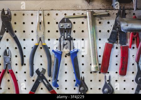 Close-up of various pliers, wire stripper hanging on white pegboard wall in home garage workshop, Quebec, Canada Stock Photo