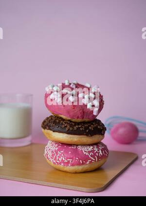 Stack of pink and chocolate glazed donuts decorated with sprinkles, served with fresh strawberries on a pastel pink background. Fun sweet dessert conc Stock Photo