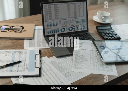 Laptop and tablet display billing spreadsheets, transaction tables, charts beside printed reports, supporting document review, accounting analysis, fi Stock Photo