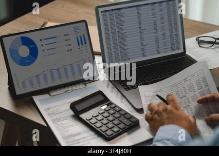 Businessman analyzing financial data charts on tablet, spreadsheet data on laptop, calculator, printed reports, supporting accounting analysis, financ Stock Photo