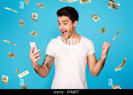 Lucky Winner. Excited Man With Smartphone Screaming With Joy Under Money Shower Stock Photo