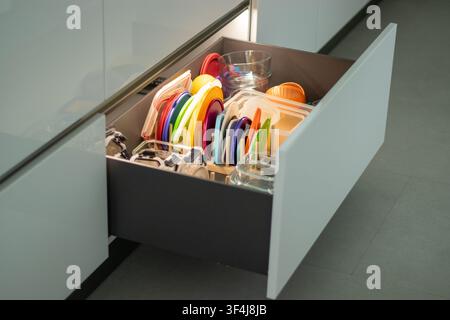 Kitchen drawer filled with colorful plastic lids, glass containers, and kitchen utensils Stock Photo