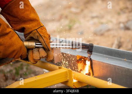 Bright sparks flying while worker cuts metal beam with torch on construction site Stock Photo