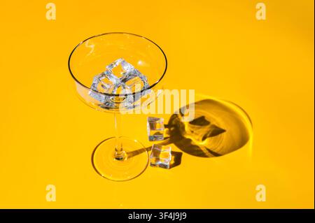 Empty cocktail glass with ice cubes on a vibrant yellow summer background. Stock Photo