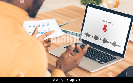 Unrecognizable African Businessman At Laptop Using Voice Assistant Indoor, Rear-View Stock Photo