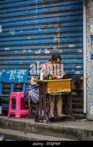 UNKNOWN, China - August 16, 2017: A woman with dark hair pulled back, wearing a red polka dot shirt, operates a black vintage sewing machine with a wo Stock Photo