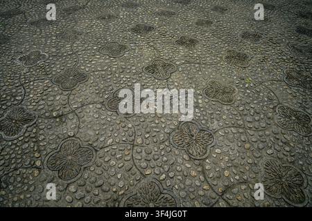 A dark gray ground is covered in small, smooth pebbles, interspersed with carved stone sections forming intricate quatrefoil shapes and flowing vine-l Stock Photo