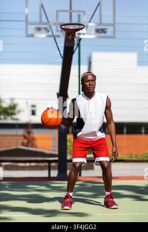 Serious black sportsman dribbling ball at basketball court outdoors Stock Photo