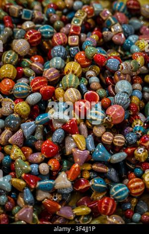 A vertical, close-up shot of numerous ceramic beads in various shapes, sizes, and colors, including round, oval, square, and triangular forms. The bea Stock Photo