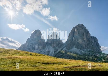 View of the Sassolungo mountain group with bright sunstar and grassy alpine meadow at Passo Sella. Val Gardena, Dolomites, Trentino South Tyrol, Italy Stock Photo
