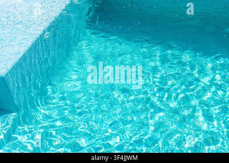 Sunlight dances on the clear, blue water of a tiled swimming pool, creating mesmerizing patterns and reflections Stock Photo