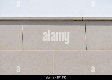 A close-up view of a building exterior showcasing a contrast between rough white plaster and smooth beige stone cladding Stock Photo
