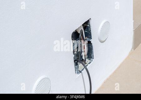 Close-up view of an open electrical box with visible wires and two round ventilation grilles on a textured white wall Stock Photo