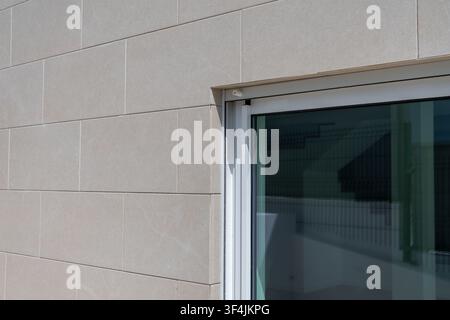 Close-up view of a contemporary building exterior featuring light-colored, rectangular stone cladding and a sleek, reflective glass window Stock Photo